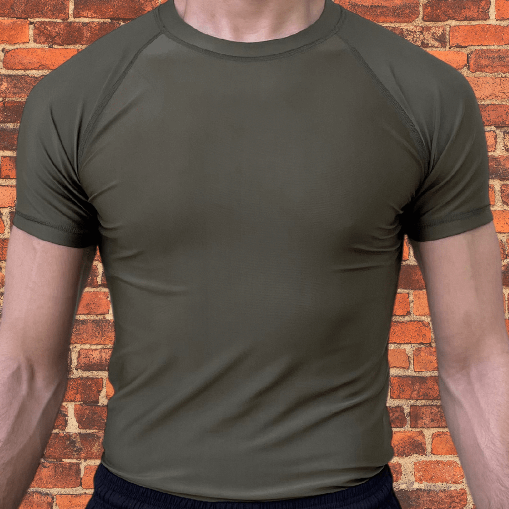 Front view of a plain Toro BJJ Olive Drab Rash Guard with short sleeves and a minimalist design against a brick wall background.