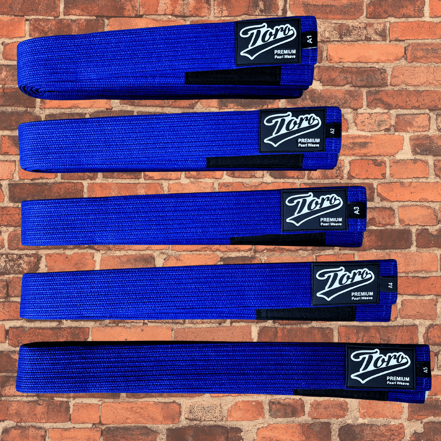 Premium pearl weave BJJ Blue belt with Toro logo patch and black rank bar on brick background