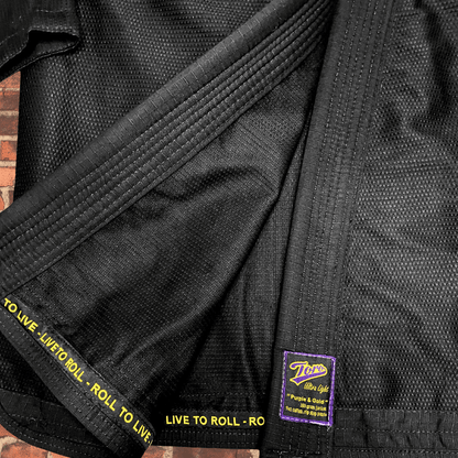 Closeup of black BJJ Gi fabric with Toro purple and gold patch and Live to Roll trim, IBJJF approved Purple & Gold Gi