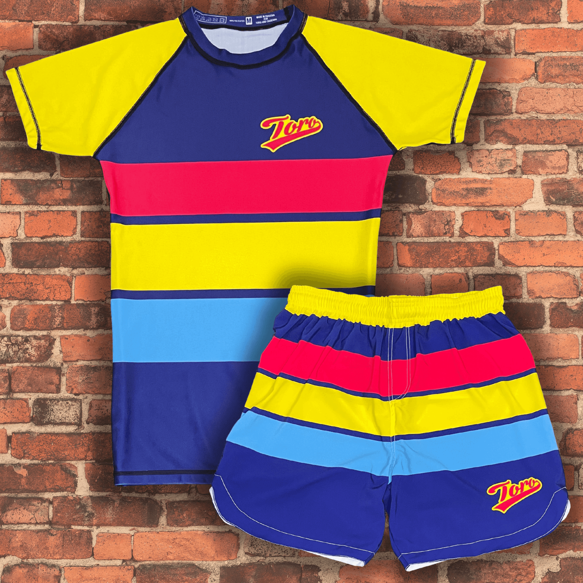Toro BJJ Summertime NoGi kit featuring a colorful rash guard and matching shorts with red, yellow, blue, and navy stripes.