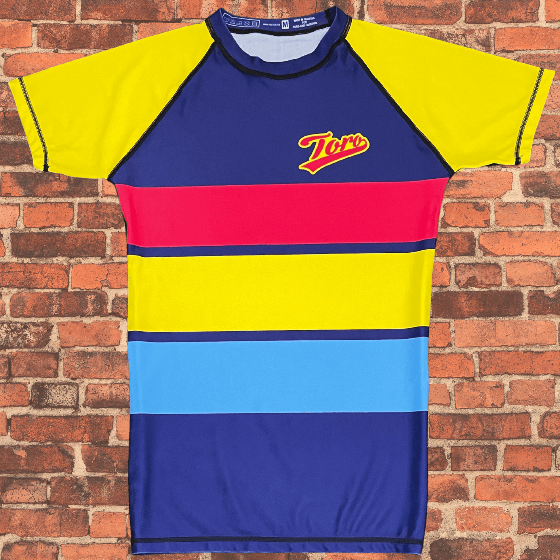 Toro BJJ Summertime Rash Guard featuring bold yellow, red, and blue stripes with Toro logo on the chest.