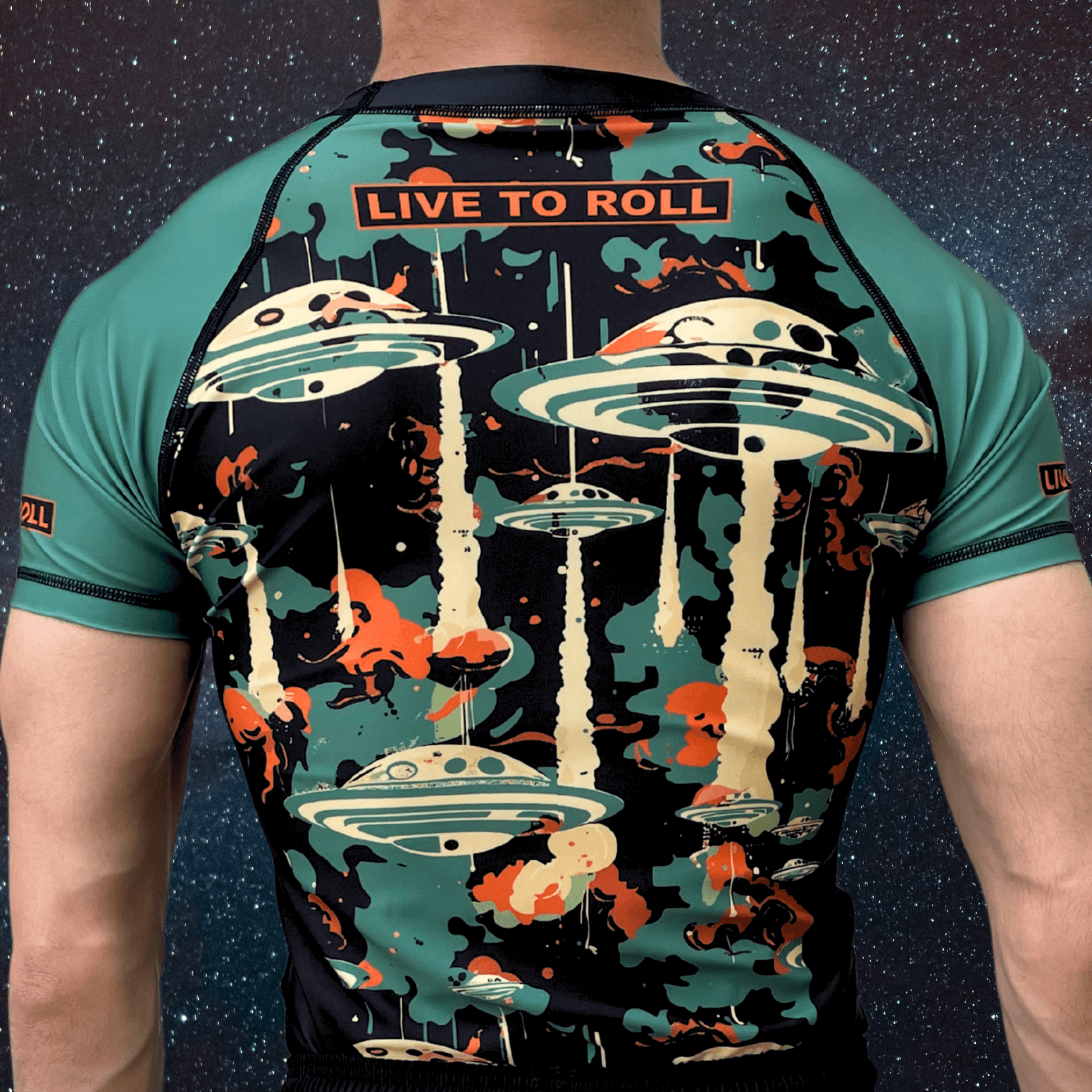 Back view of Toro BJJ Cosmic Rash Guard with “Live to Roll” text and UFO design in green, orange, and black tones