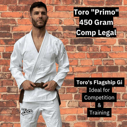 Male athlete wearing the Toro Primo white BJJ Gi with brown belt, standing against a brick wall. Overlay text highlights it as a 450 gram, comp-legal flagship gi ideal for training and competition.
