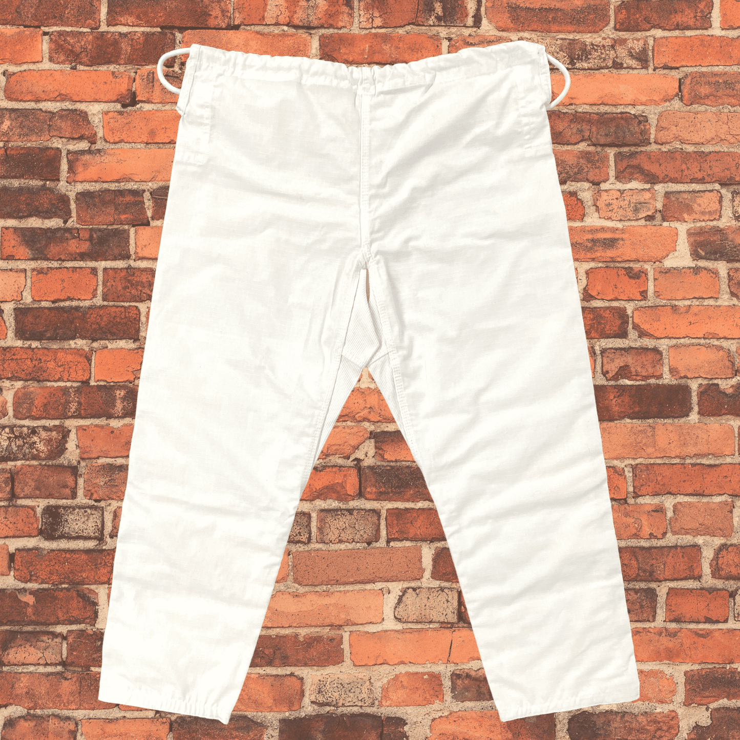 Back view of white Toro BJJ gi pants with elastic drawstring waistband and reinforced seat area, shown against a red brick wall.