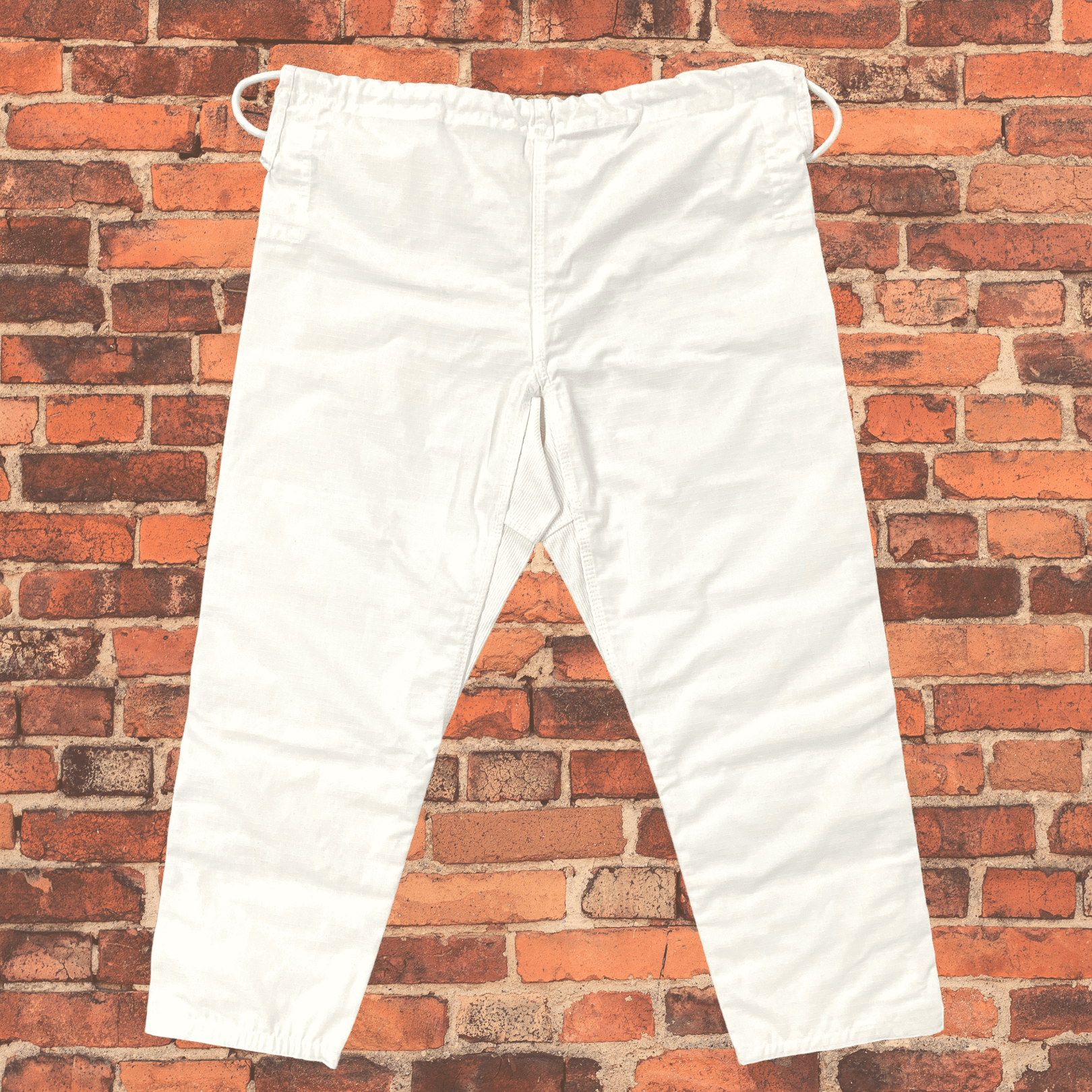 Back view of white Toro BJJ gi pants with elastic drawstring waistband and reinforced seat area, shown against a red brick wall.
